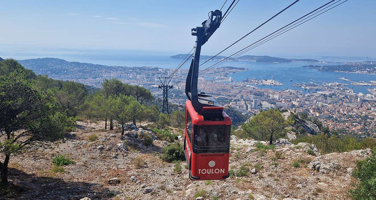 The red Toulon cable car climbing toward Mont Faron with the city's harbor spread out below