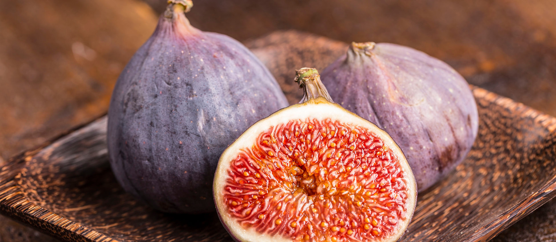 Whole and halved Violette de Solliès figs showing deep purple skin and ruby-red flesh on a rustic wooden tray