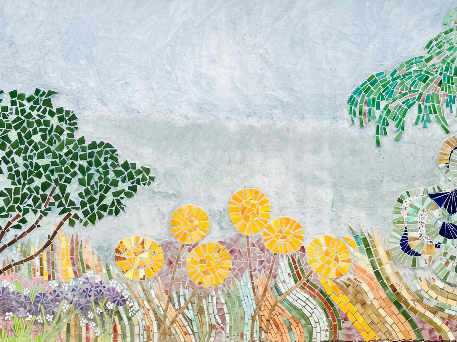 Colorful ceramic mosaic mural of flowers, trees and a seated figure in Salernes