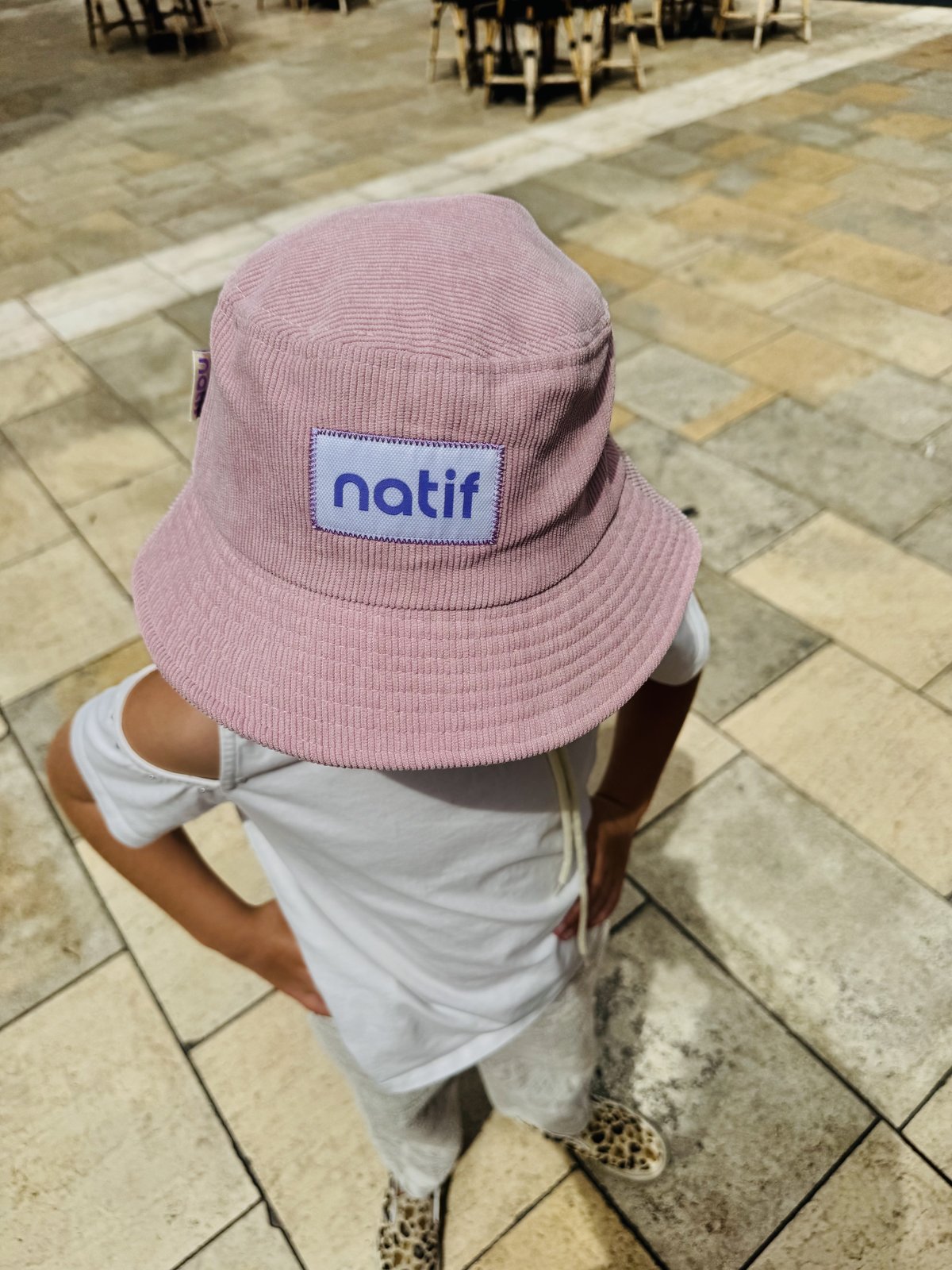 A pink Natif corduroy bucket hat with the brand's woven label, worn on a tiled terrace