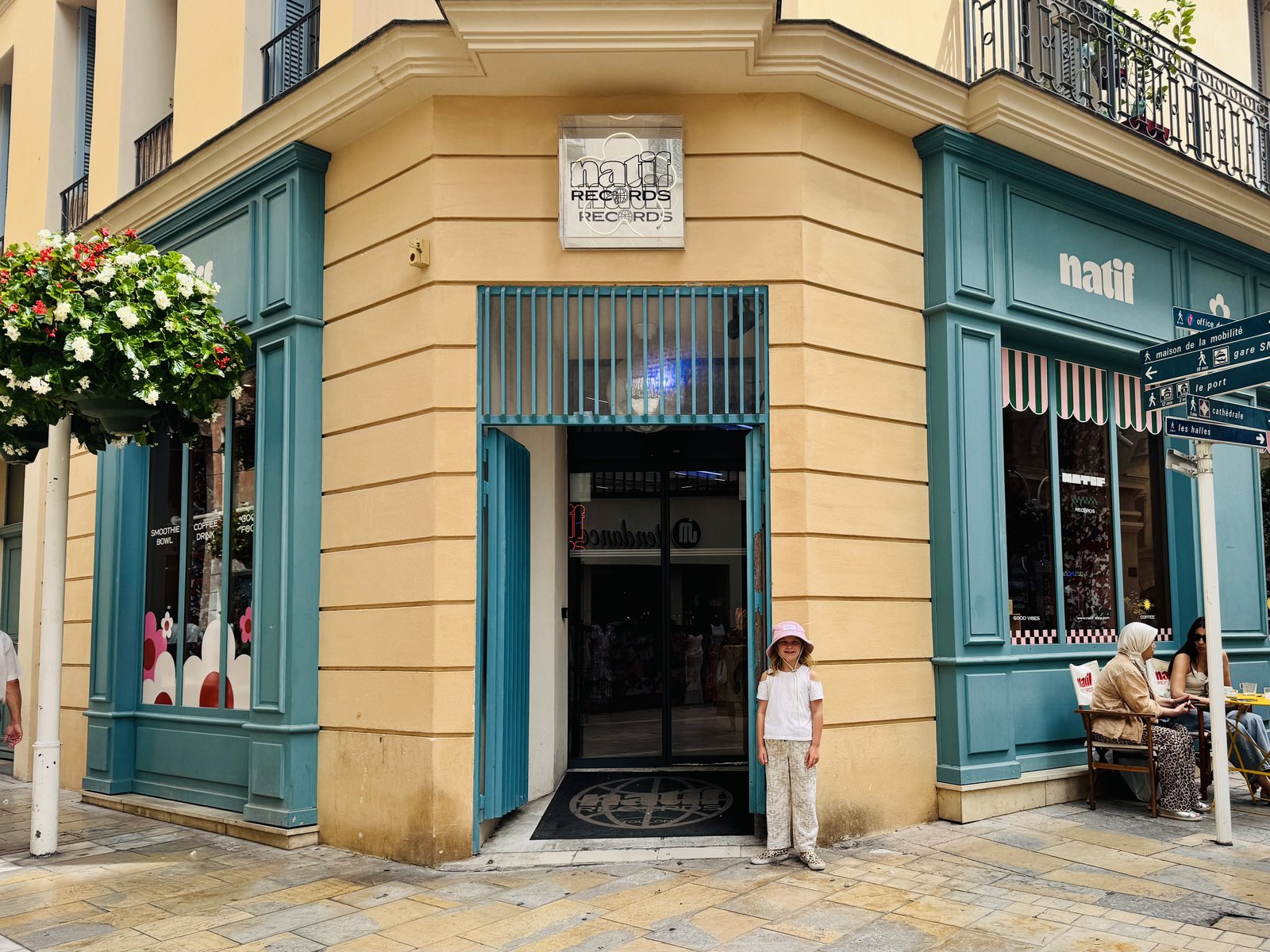 The teal and yellow Natif storefront on a street corner, with a young shopper in a pink Natif bucket hat outside