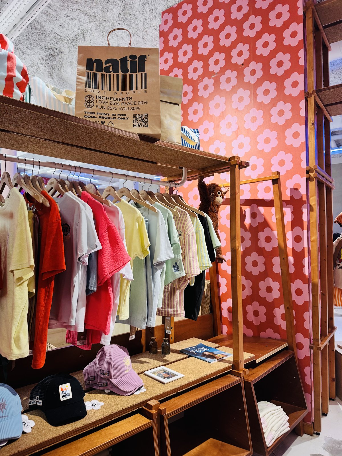 Pastel Natif t-shirts and corduroy caps on wooden racks inside the boutique, under a flower-print wall