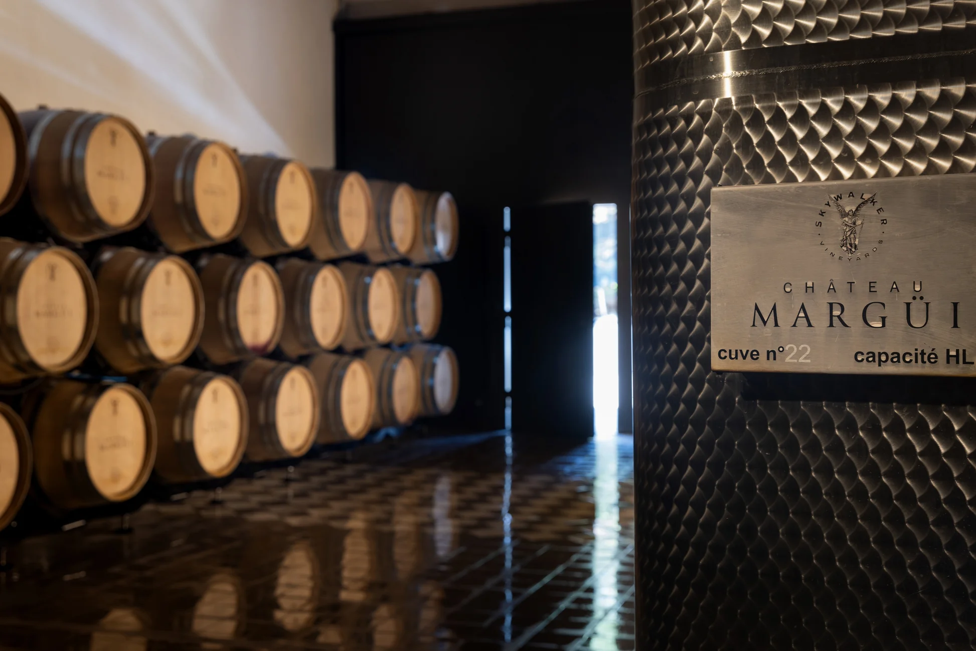 Oak barrels and a stainless steel tank marked Château Margüi in the winery's cellar at Châteauvert