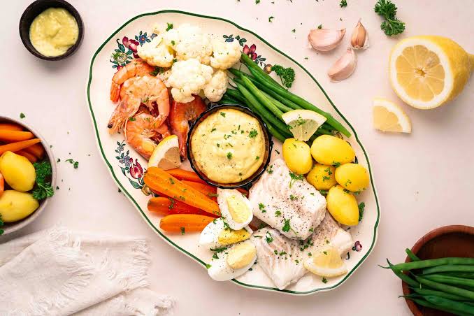 Traditional Provençal grand aïoli platter with salt cod, shrimp, boiled vegetables, eggs, and a bowl of garlic mayonnaise at the center